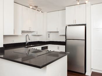A kitchen with white cabinets and a black counter top at Skye at Belltown Apartments, Washington